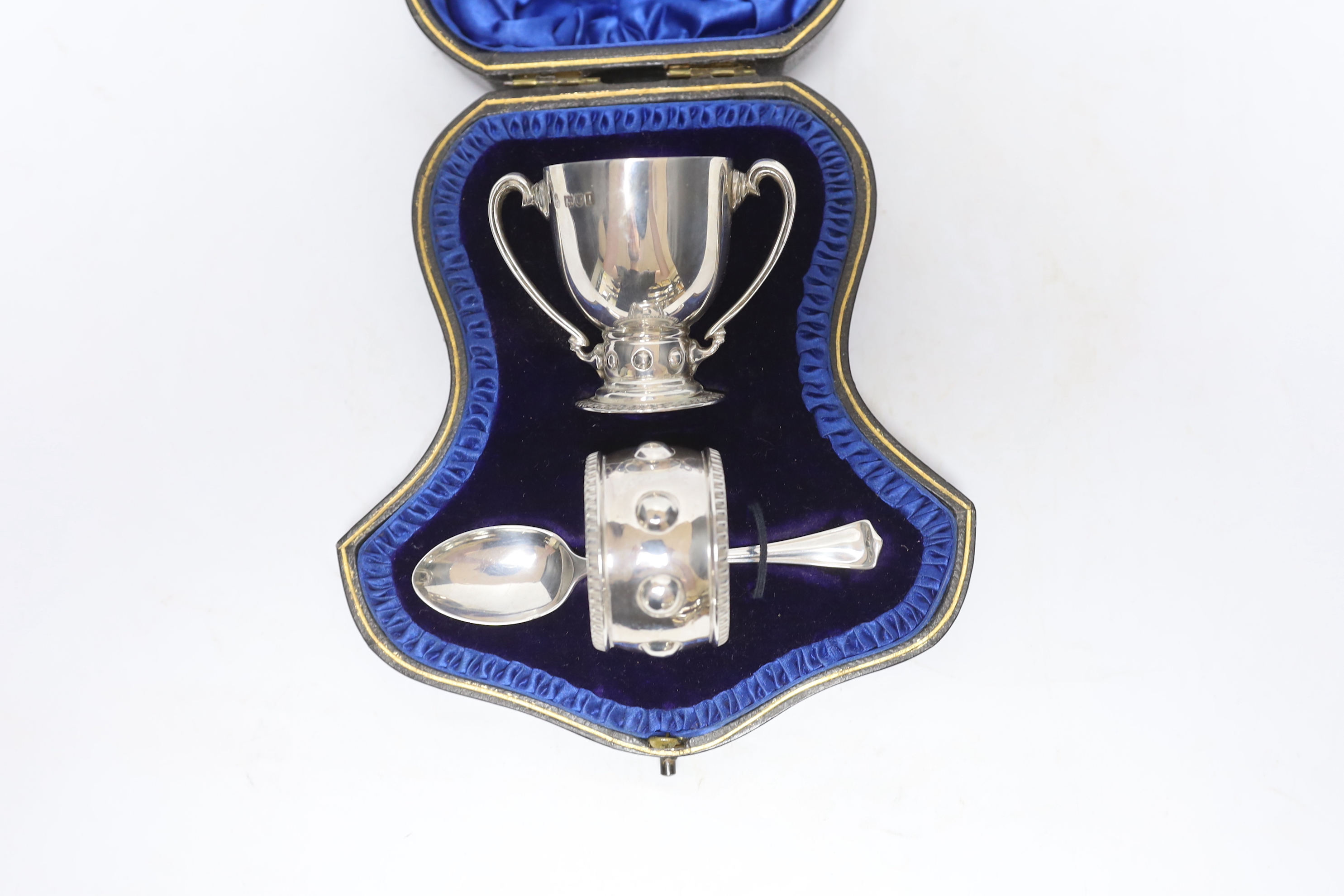 A cased Edwardian matched silver christening pair, (egg cup and napkin ring), Wakeley & Wheeler, London, 1905/6, with associated silver spoon.